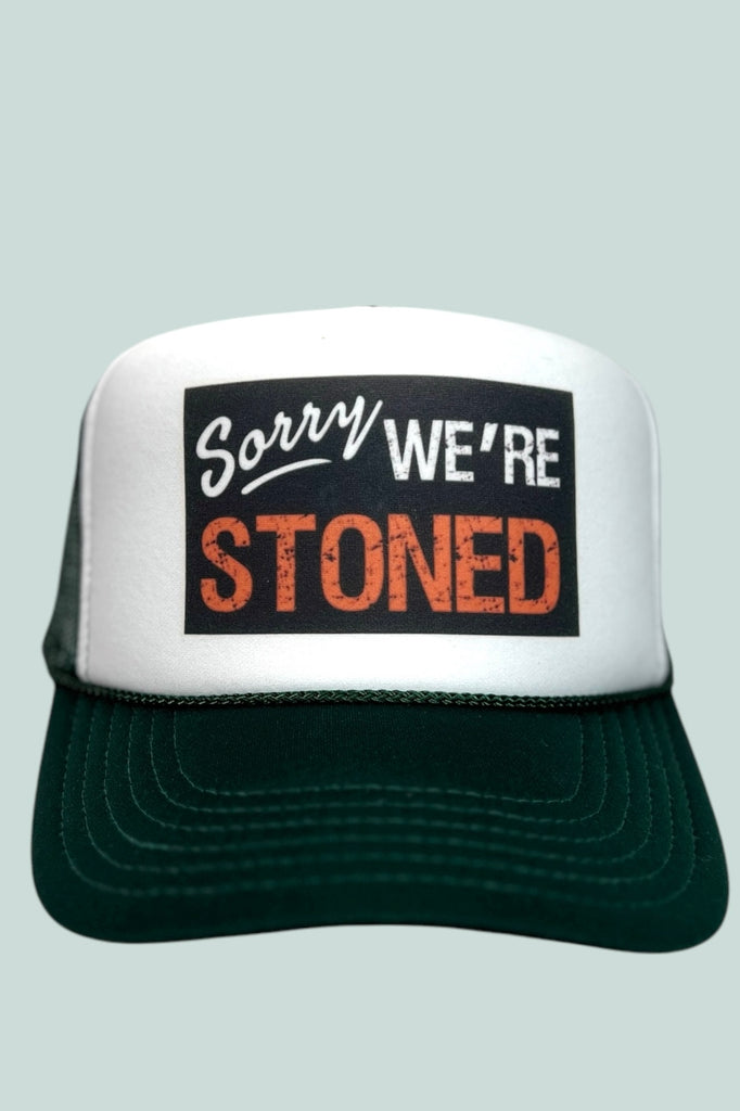 Green and white foam front trucker hat with "Sorry we're STONED" printed across  the front. 