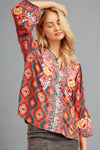A women’s relaxed fit bell-sleeve blouse with split scoop neck featuring floral embroidery overlaying an aztec print in red, teal, and pink.