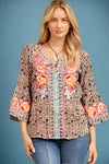 A women’s relaxed fit bell-sleeve blouse in a blush color with all over black geometric print featuring a notched scoop neck and floral embroidery along front and sleeves.