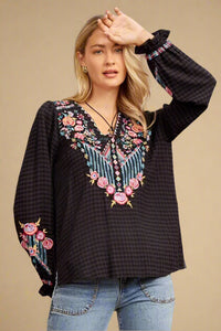 Savanna Jane embroidered v-neck long sleeve blouse. Southwestern floral embroidered detail over black and grey checkered pattern.