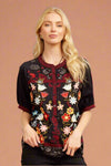 A women’s floral embroidered blouse featuring mandarin collar and half button front. Short sleeves with embroidered trim along hem and button front.