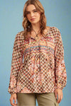 A long sleeve, tie front blouse. It has a mix of neutral colors in the geometric pattern including brown, rust, ivory, and teal.