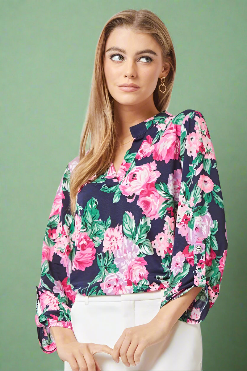 A womens lightweight, loose fit top with split v-neckline featuring a slight high-low hem, 3/4 sleeve length, and brightly colored pink and green floral print over navy blue base.