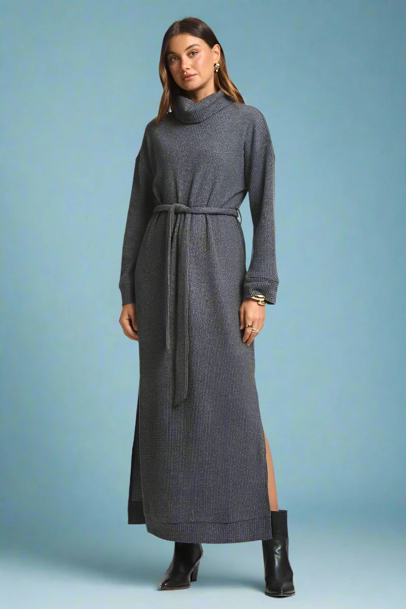 Woman wearing a long gray dress with a belt on a plain background.