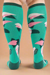 Green knee-high socks with pink and black floral pattern worn by a person on a white background