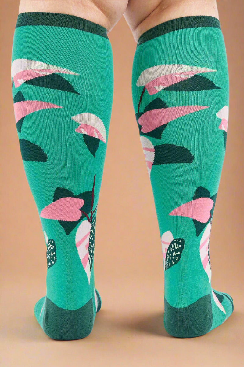 Green knee-high socks with pink and black floral pattern worn by a person on a white background