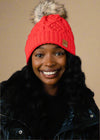 Person wearing a red knit beanie with a pom-pom on a black background