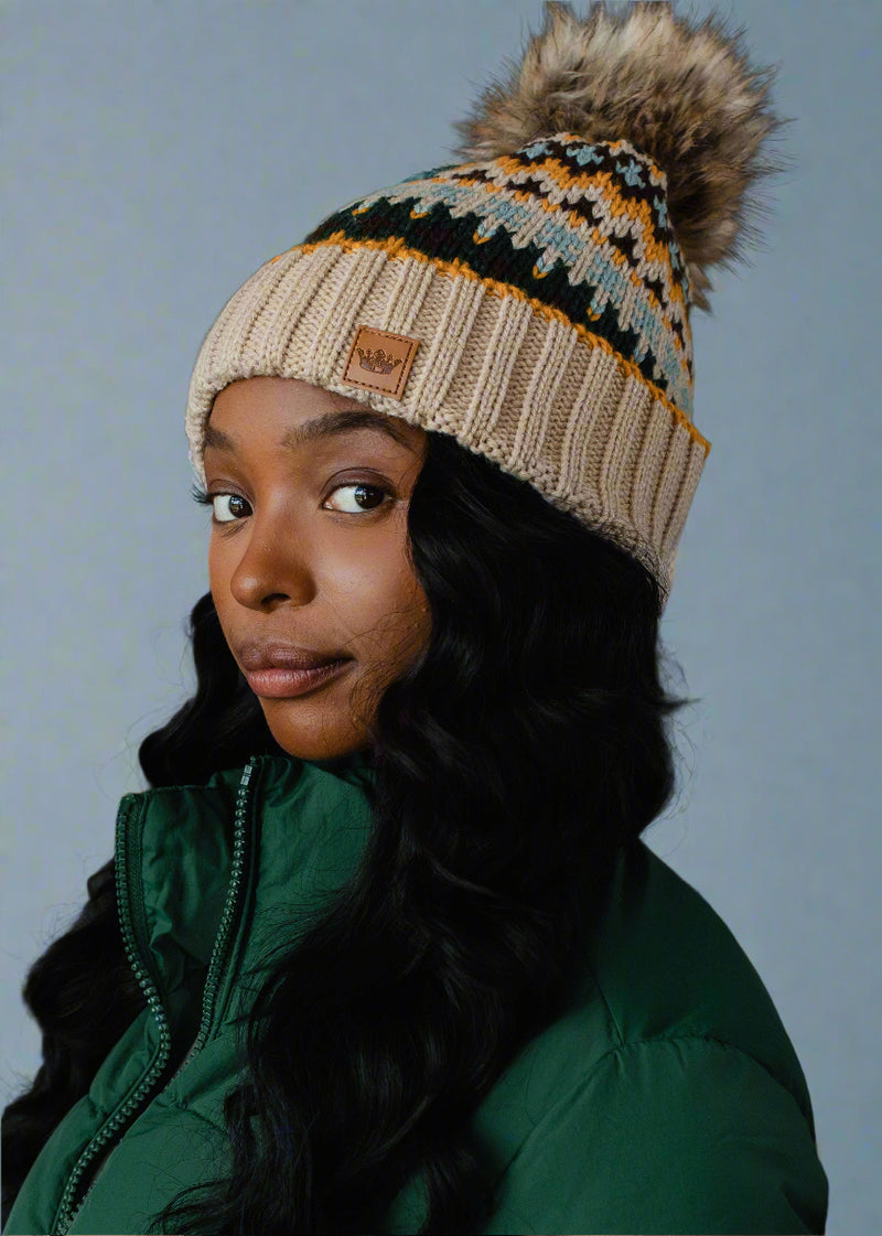 Woman wearing a patterned knit beanie with a pom-pom against a dark background