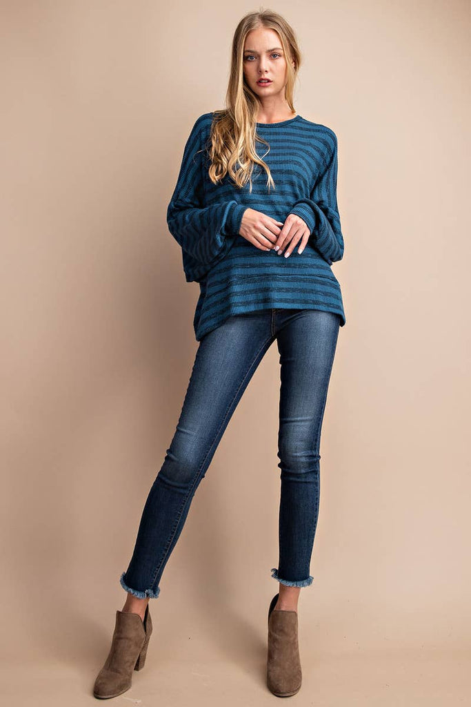 Model is wear a teal striped top. The flowy top features a dolman sleeve, round neck and open back. The back has a tie at the neck and a playful criss cross detail. 