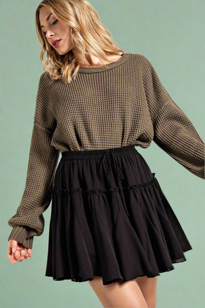 Model is wearing a solid black mini skirt with elastic tie waist and ruffle detail. 