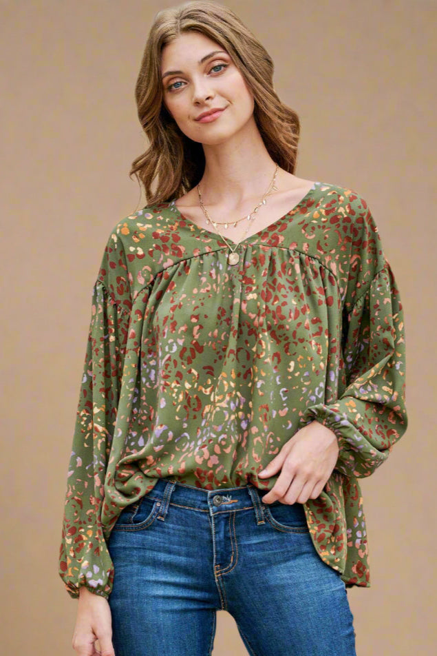 Model is wearing a loose fitting baby doll top in olive. The top features a multi color leopard print with a v neck. 