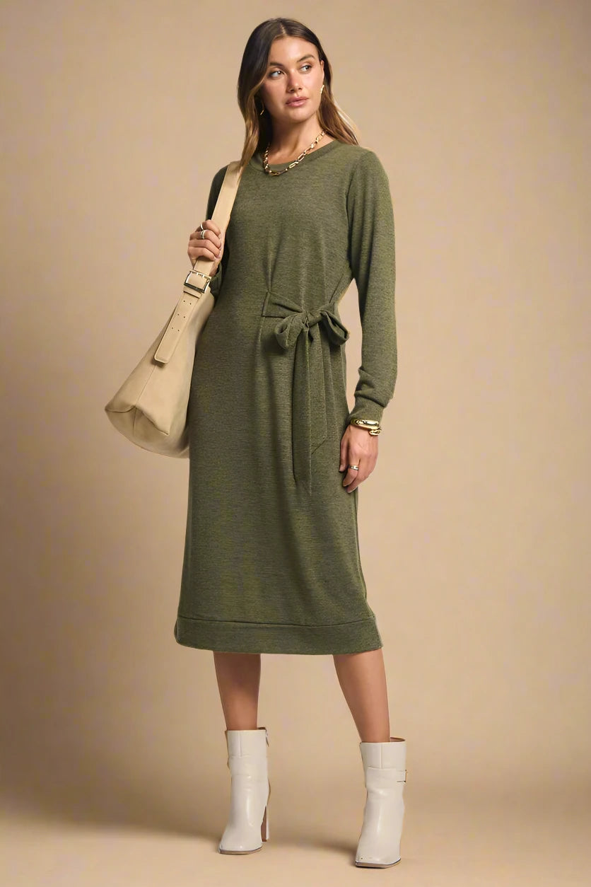 Woman wearing a green dress with a beige bag and boots on a plain background