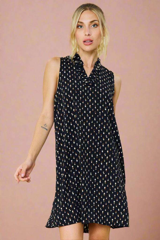 Model is wearing a black sleeveless dress with an abstract print. The dress features a v neck with a ruffle detail. 