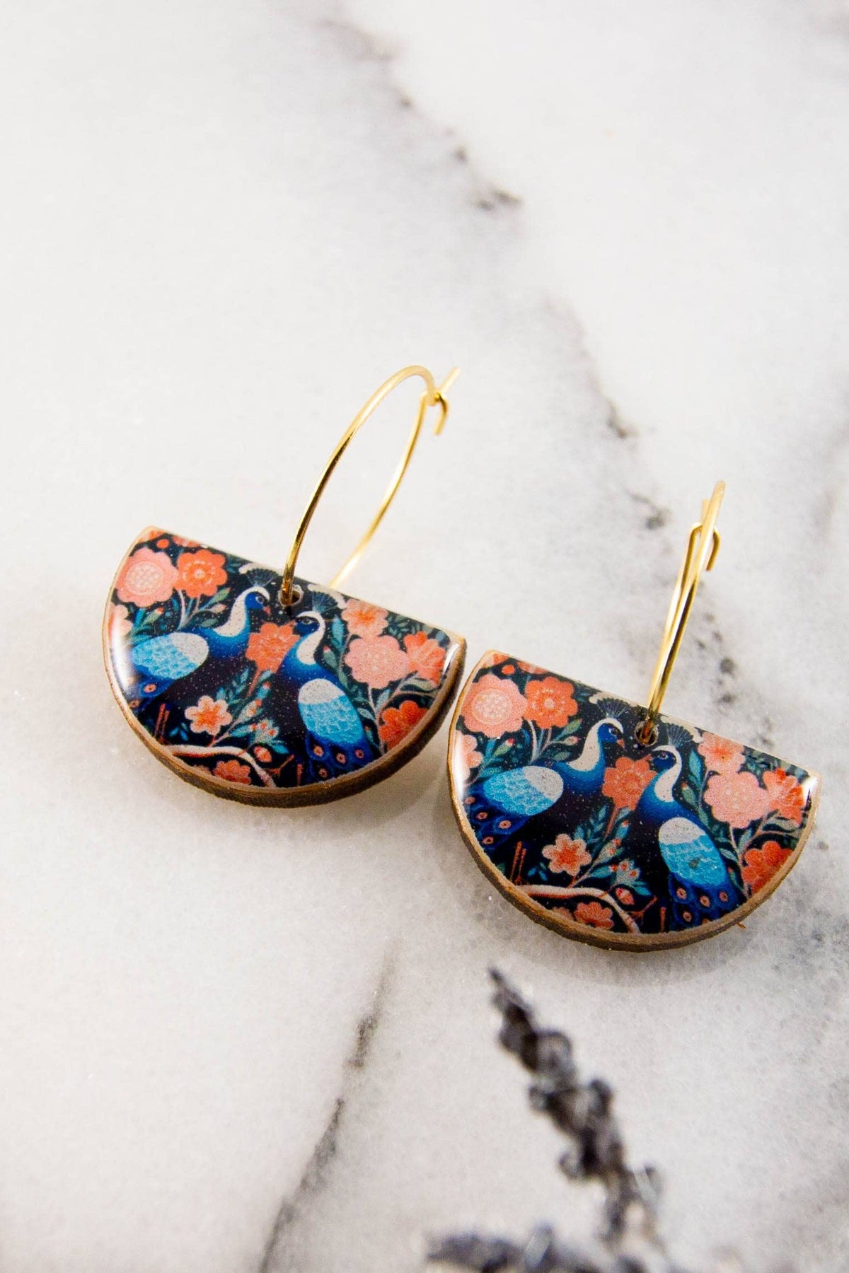 A pair of drop hoop earrings featuring colorful peacock and flowers. They are made from BPA/VOC free resin. 
