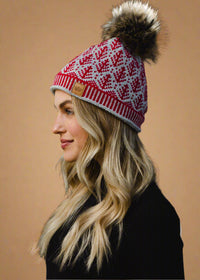 Woman wearing a red and white patterned knit hat with a pom-pom against a black background