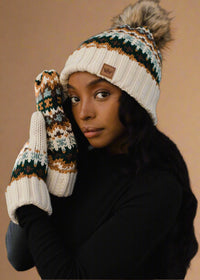 Person wearing a patterned knit hat and mittens against a black background