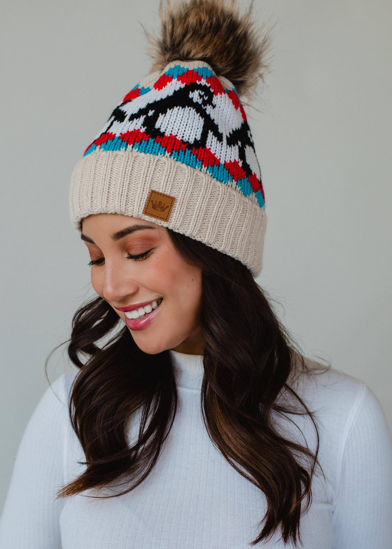 Woman wearing a colorful knit beanie with a pom-pom on a plain background
