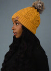 Woman wearing a yellow knit beanie with a pom-pom on a black background