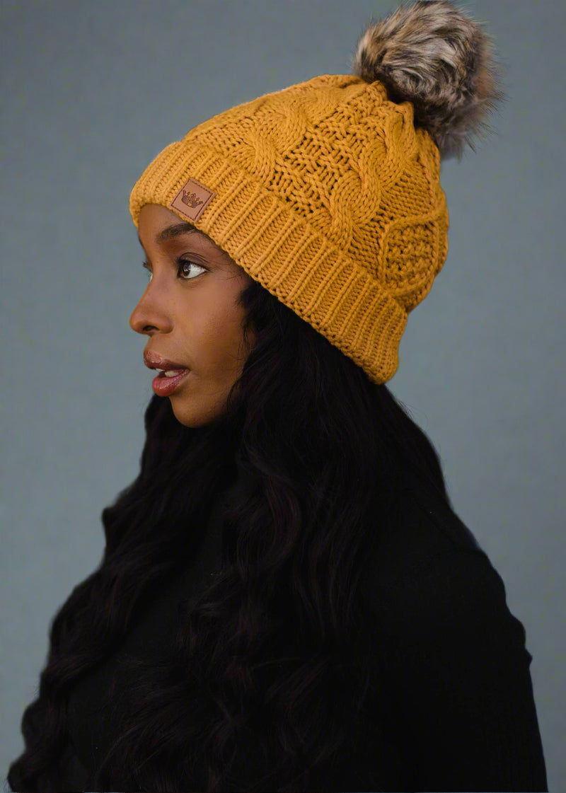 Woman wearing a yellow knit beanie with a pom-pom on a black background