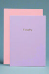 A minimalist greeting card in lavender with small gold text that reads ‘Finally.’ and a pink envelope.