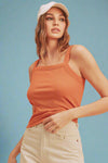 Woman wearing an orange tank top and beige shorts against a beige background