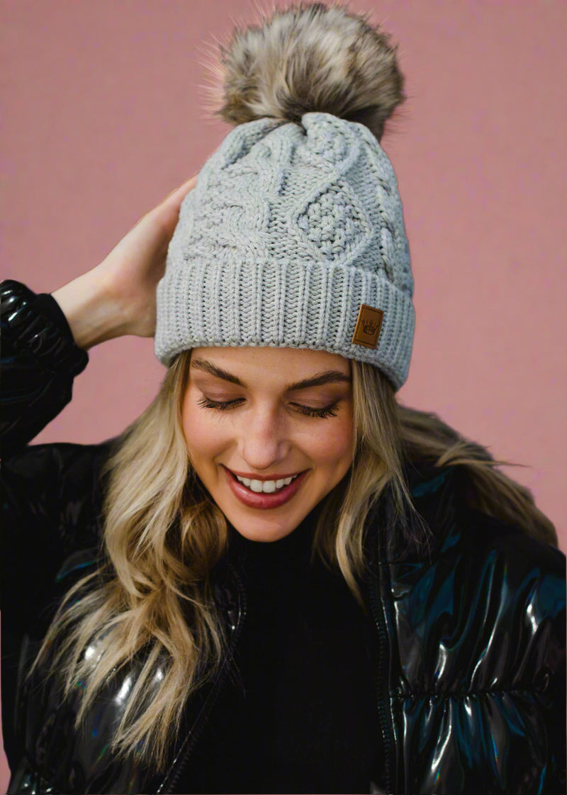 Woman wearing a gray knit beanie with a pom-pom against a black background
