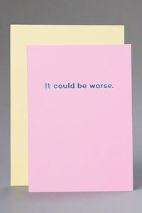 A solid pink greeting card with metallic blue text that reads ‘It could be worse.’