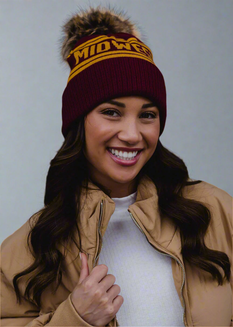 Woman wearing a maroon beanie with 'Mid West' text, tan jacket, and white shirt against a black background
