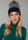 Woman wearing a black and gray striped beanie with a fur pom-pom against a neutral background