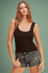 Woman wearing a black tank top and denim shorts against a beige background