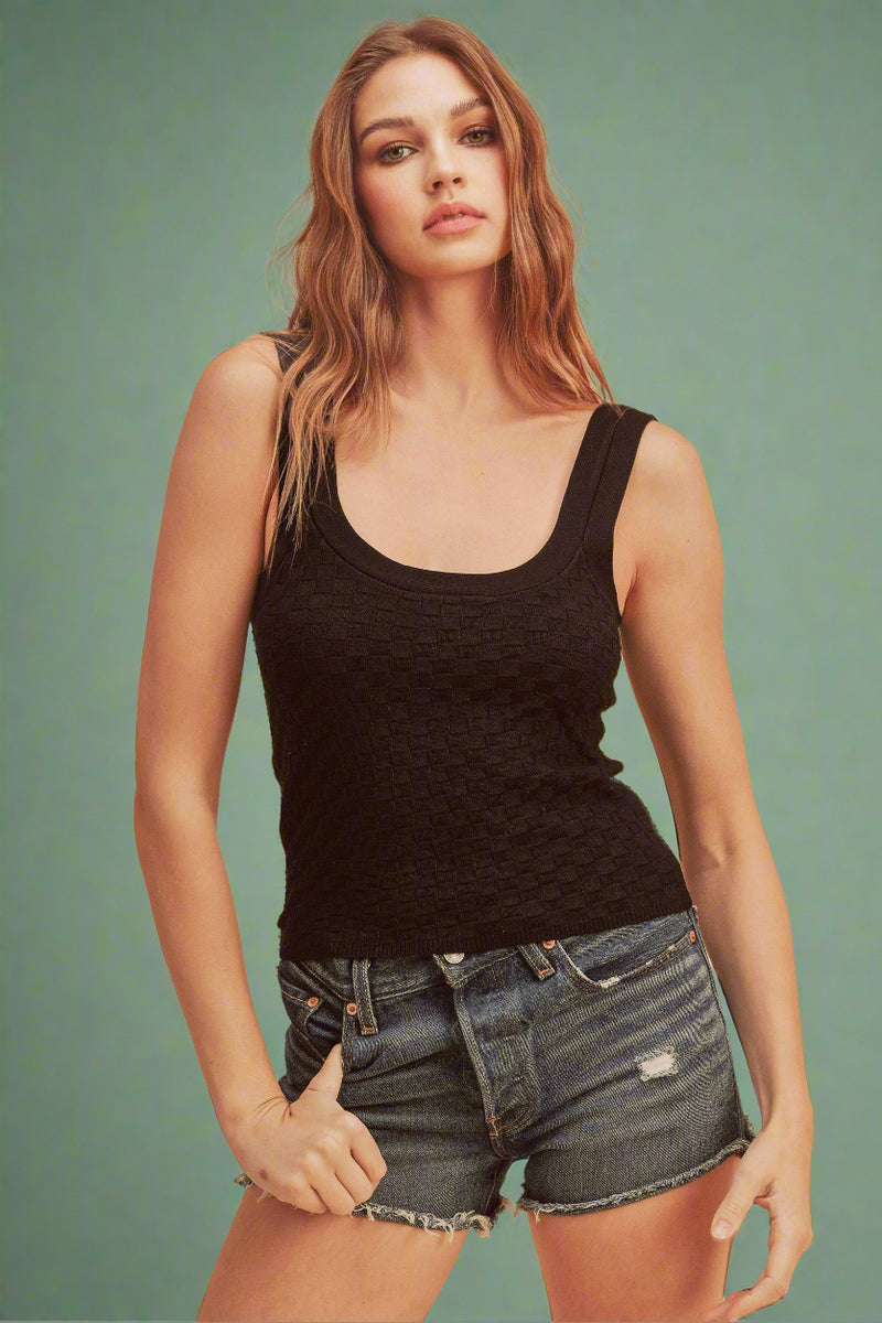 Woman wearing a black tank top and denim shorts against a beige background