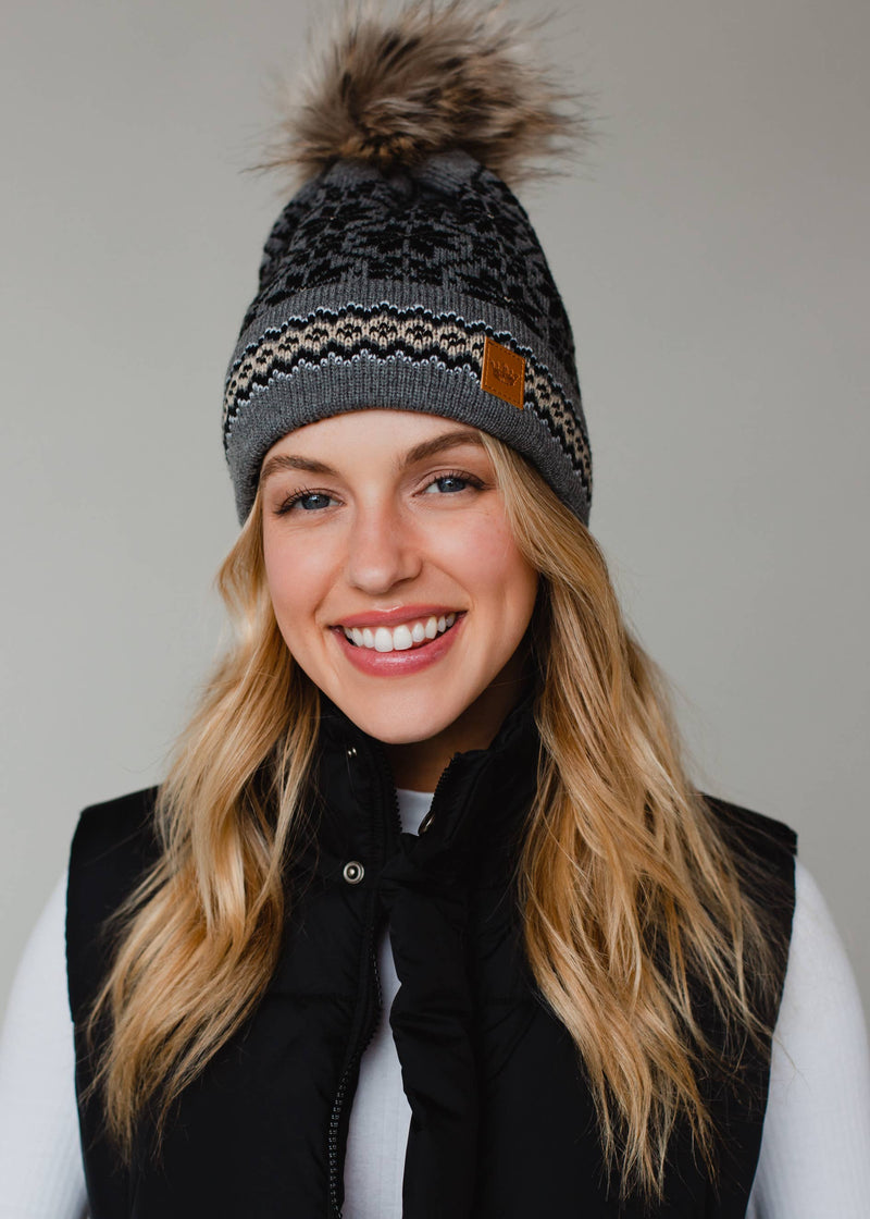 Woman wearing a patterned beanie with a pom-pom on a plain background