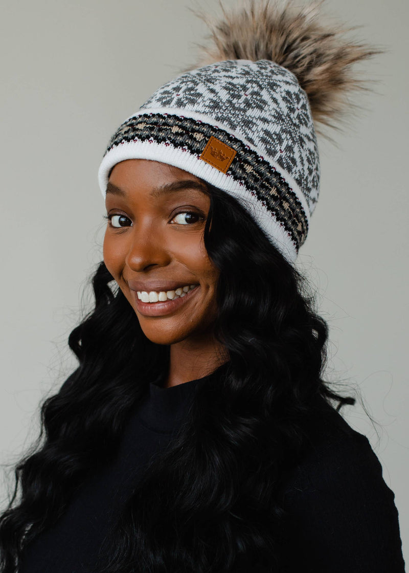Woman wearing a patterned beanie with a pom-pom on a plain background