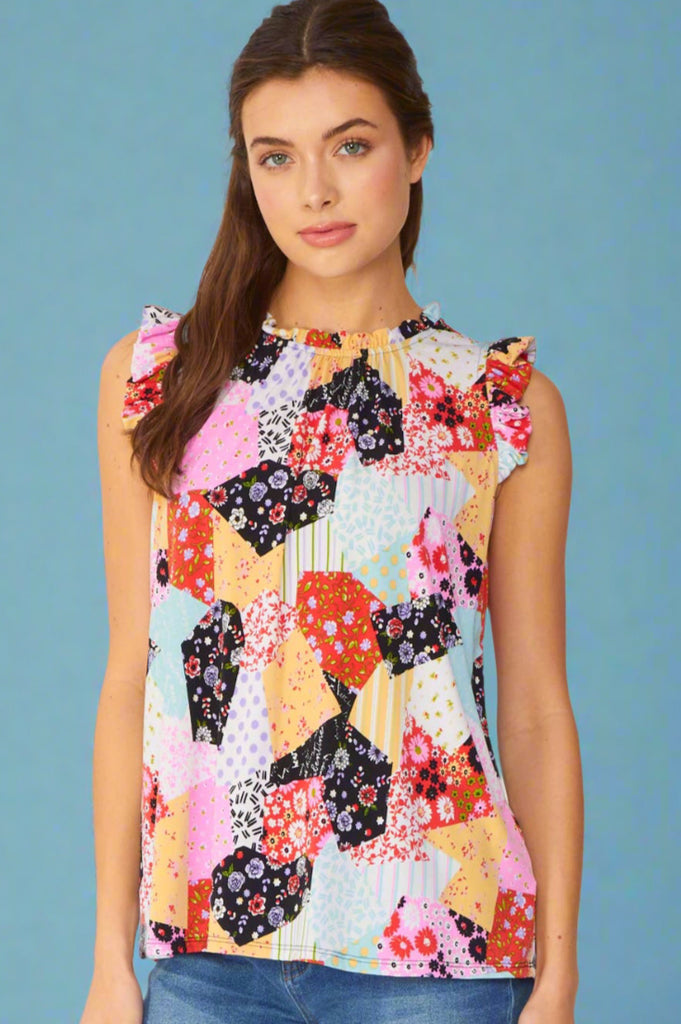 Model is wearing a cute patchwork top with ruffle neck and arm details. The top is sleeveless with a long line. Features a mix of patterns primarily pink and floral. 