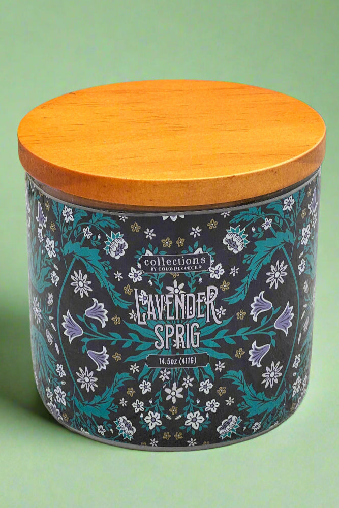 A lavender sprig scented candle in a glass jar with decorative ‘wallpaper’ wrap and wood lid.
