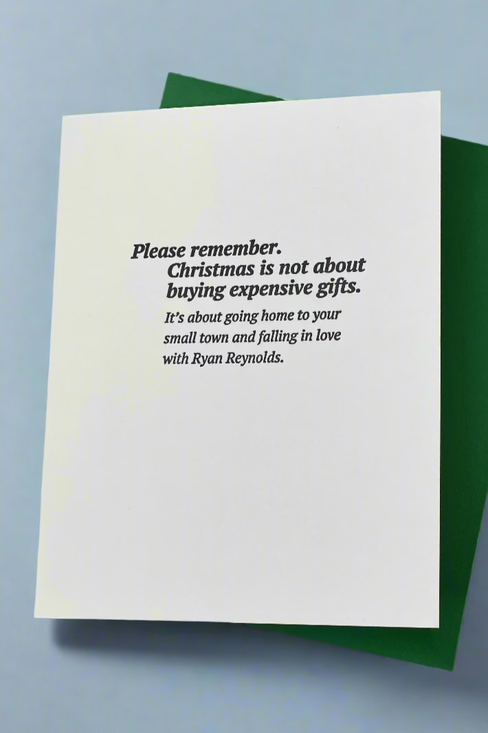 A white card with the words “Please remember. Christmas is not about buying expensive gifts. It’s about going home to your small town and falling in love with Ryan Reynolds.”