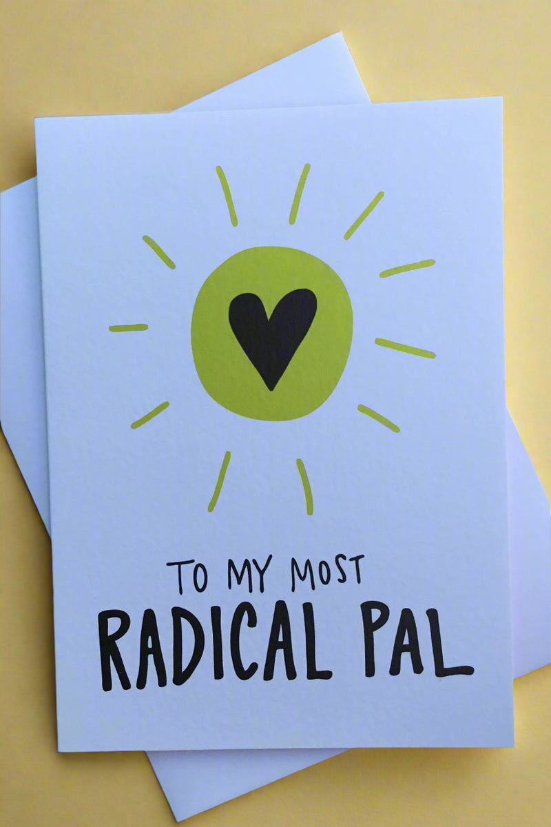 A white card with a black heart in a green sunburst that says “to my most radical pal.”