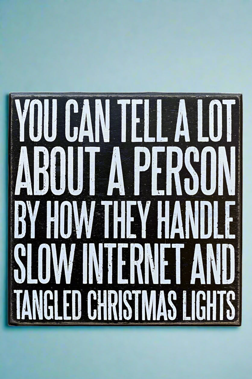 A square black sign that says “You can tell a lot about a person by how they handle slow internet and tangled Christmas lights” written in white.