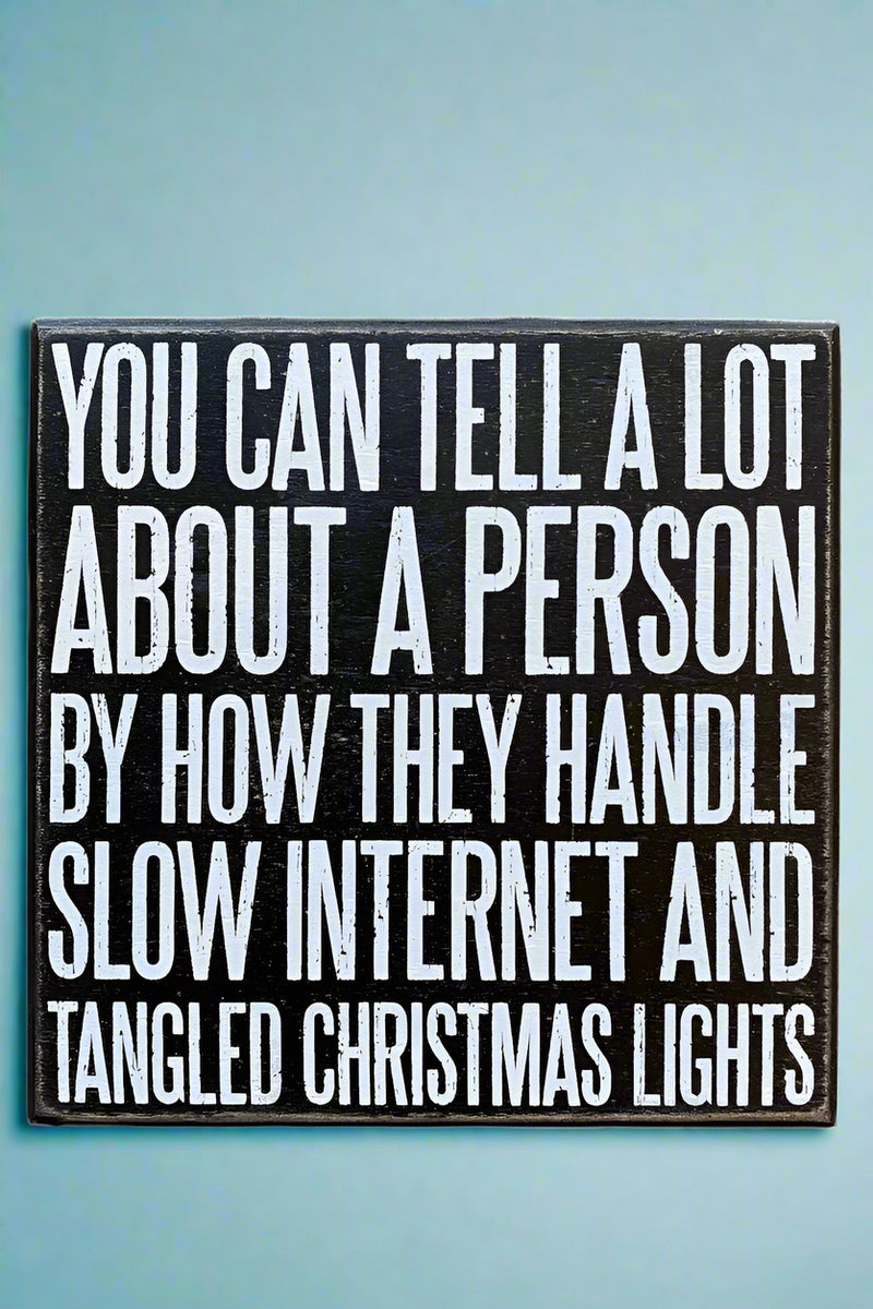 A square black sign that says “You can tell a lot about a person by how they handle slow internet and tangled Christmas lights” written in white.