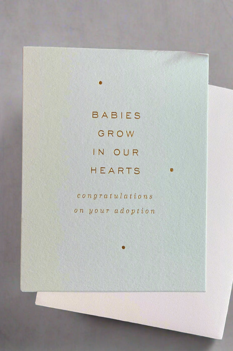 The front of a greeting card that says, ‘Babies Grow In Our Hearts. Congratulations on your adoption.’ 