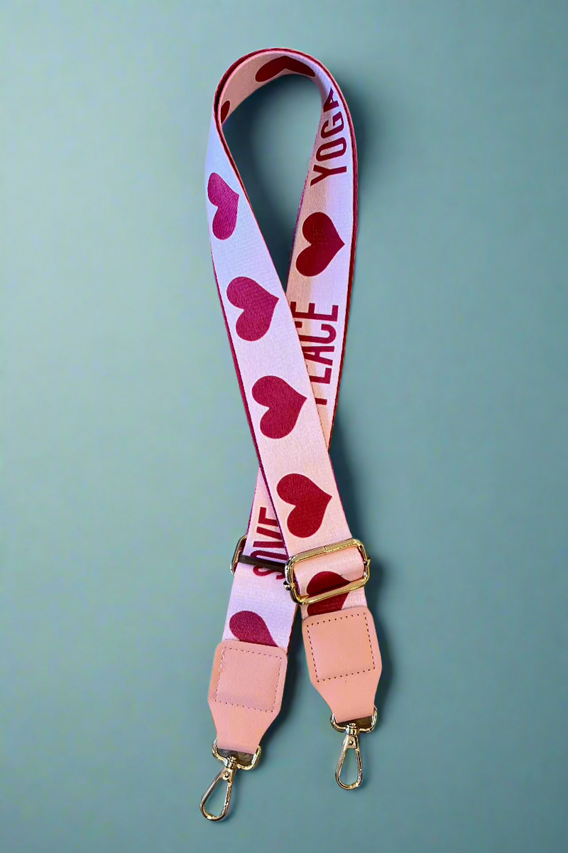 A guitar strap for purses that has the words ‘Peace Love Yoga’ and heart decals in red.