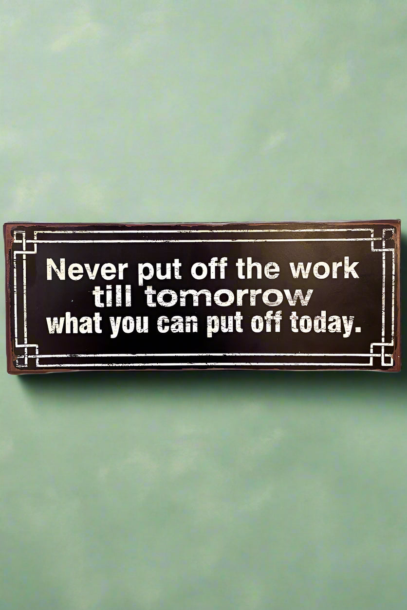 A black metal sign with old proverb printed on it in white that states ‘Never put off the work till tomorrow what you can put off today.’