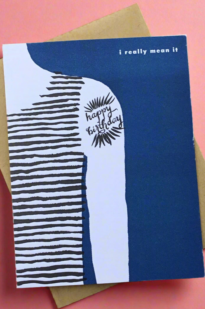 A blue greeting card with an illustration of half of someone’s torso and arm with tattoo of happy birthday and the text ‘I really mean it’.