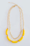 The Holly necklace is layered with a shorter, chain link pattern while the longer chain is strung with several yellow, elongated beads.