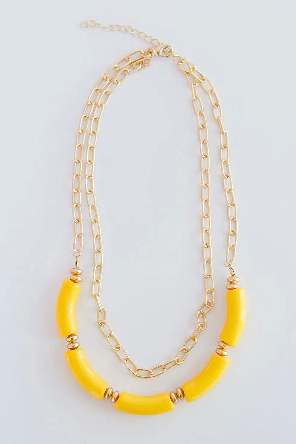 The Holly necklace is layered with a shorter, chain link pattern while the longer chain is strung with several yellow, elongated beads.