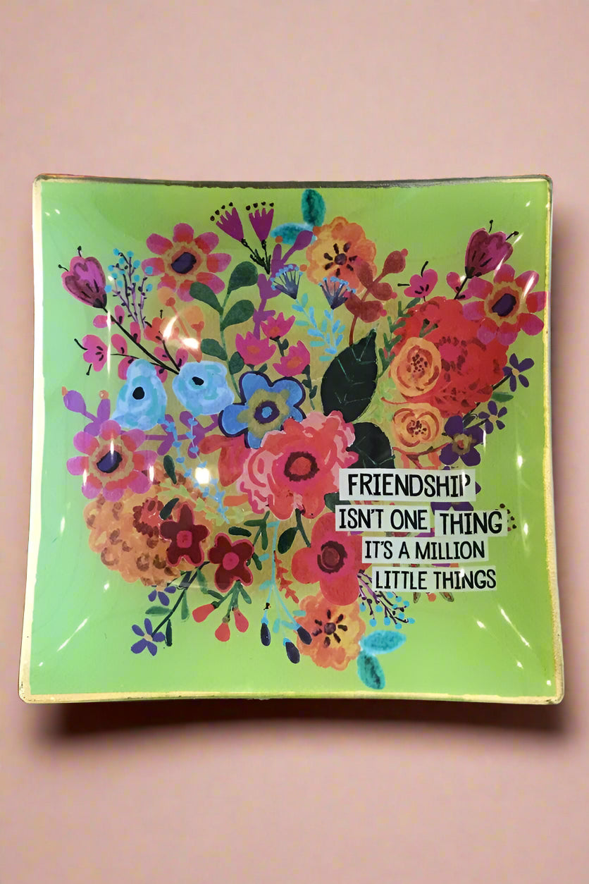 Little glass catch-all plate with green background and bright floral design that reads ‘Friendship isn’t one thing, it’s a million little things.’