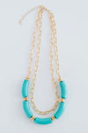 The Holly necklace is layered with a shorter, chain link pattern while the longer chain is strung with several teal, elongated beads.