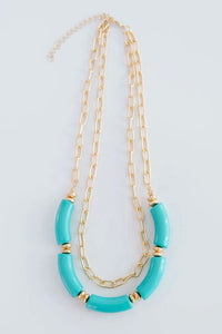 The Holly necklace is layered with a shorter, chain link pattern while the longer chain is strung with several teal, elongated beads.