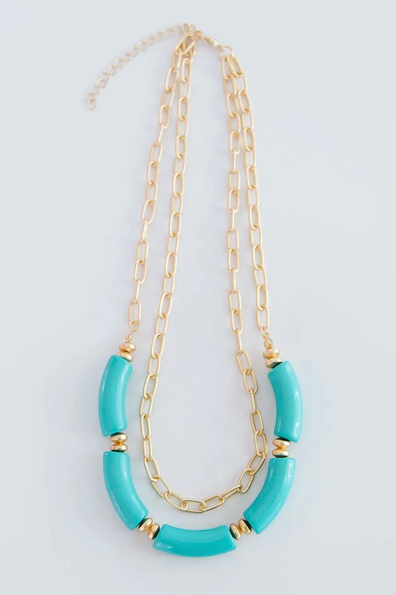 The Holly necklace is layered with a shorter, chain link pattern while the longer chain is strung with several teal, elongated beads.