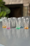 A set of six shooter glasses each with a different color base.